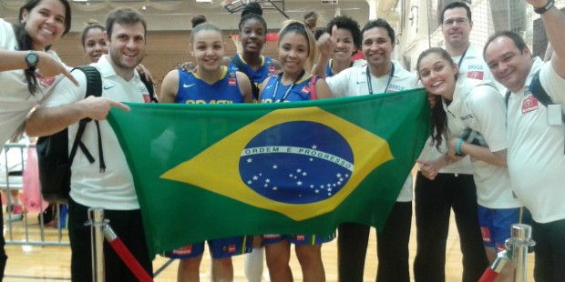 Imagem: Professor do curso de Educação Física juntamente com o time de basquete feminino sub-19 e Comissão técnica segurando a bandeira do Brasil